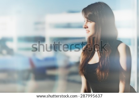 Young brunette woman is looking through the window on the planes and waiting to departure in the airport. Double exposition.
