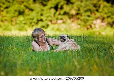 Nice blonde and cheerful young woman with her dog resting on green lawn in the park.