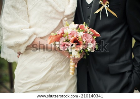 Wedding couple torsos with brides bouquet from orange calla lilies and freesia. Selective focus (on a bouquet).