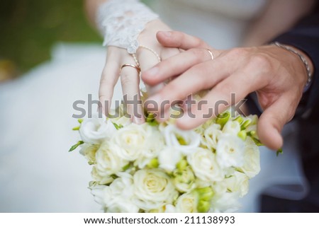 Groom and bride holding hands to reveal rings while displaying the flowers. Selective focus (on rings).