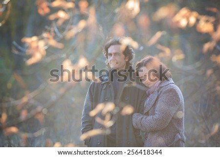 Mature couple deeply in love having a walk holding each other tight in a autumn scenery with yellow leaves.