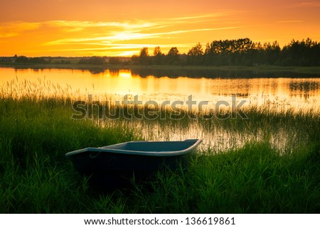 Boat on bank of river at sunset in grass