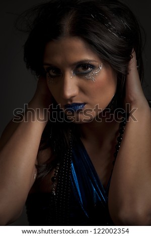 Beautiful woman with blue makeup and dress holding her dark hair away from her face