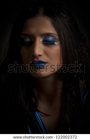 Dark portrait of mysterious woman with blue fantasy makeup
