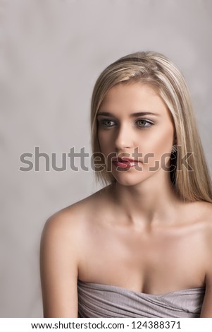 Portrait of beautiful Caucasian woman looking sideways with soft grey strapless dress, natural makeup and long blonde hair