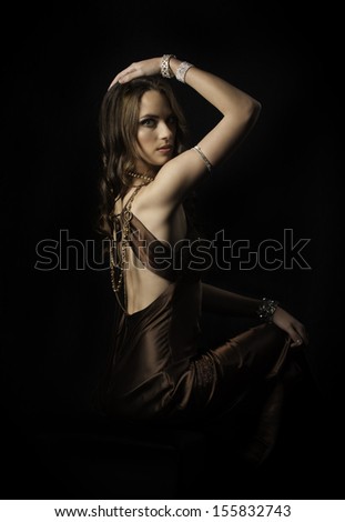 Beautiful brunette woman sitting down and wearing a satin dress with exposed back