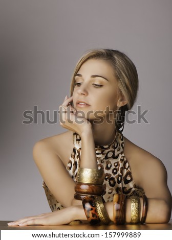 Portrait of beautiful young blonde woman resting her chin on her hand, with her long blonde hair tied back in a loose braid, wearing a leopard print top, tribal jewelry and sun kissed bronze makeup.