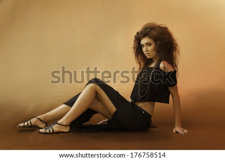 Beautiful young woman sitting down in a sexy black outfit with wild hair and gladiator sandals looking over her shoulder