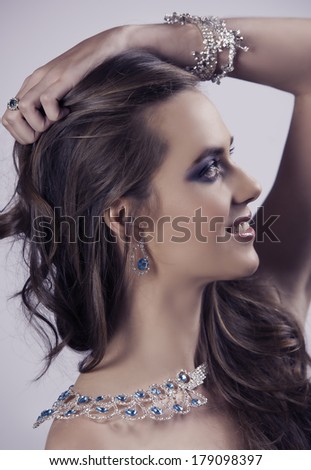 Profile portrait of beautiful brunette woman wearing diamond and sapphire jewelry posing with her hand in her hair.