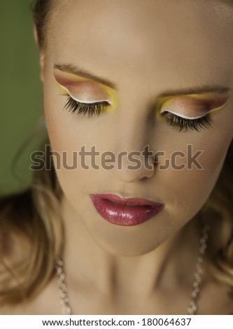 Close-up portrait of a beautiful young woman wearing white, yellow and pink makeup, who is looking down