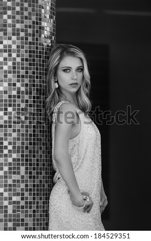 Black and white portrait of beautiful blonde woman in sexy dress leaning against mosaic pillar in city
