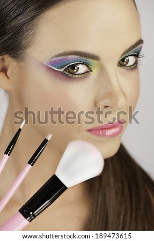Portrait of beautiful woman with colorful makeup holding up makeup brushes