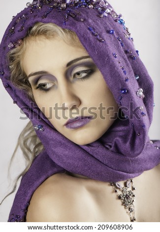 Portrait of lovely blonde woman with purple headscarf, makeup and necklace looking back over her shoulder to the side
