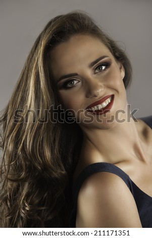 Portrait of beautiful smiling woman wearing navy dress, red lipstick and her brunette hair in a long, loose and curly style