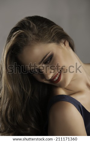 Portrait of beautiful smiling woman wearing navy dress, red lipstick and her brunette hair in a long, loose and curly style, looking back down over her shoulder
