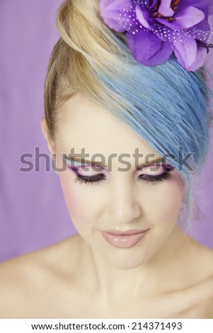 Beautiful young woman wearing her blonde and blue hair in an up-do with purple hair accessory, while looking down to expose her purple eyeshadow shot against a purple background
