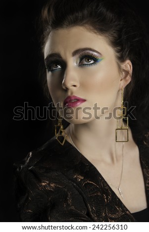 Portrait of beautiful young brunette woman looking up in eighties colorful graphic makeup wearing gold earrings.