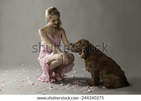 Blonde woman in pink petting her adorable dog, seated on the floor amongst pink rose petals.