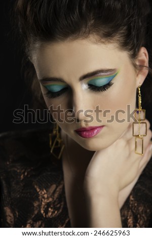 Portrait of beautiful woman with colorful makeup holding her hand to her neck while looking down.