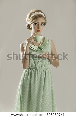 Portrait of a beautiful fifties woman with blonde hair in a retro hairstyle wearing a mint green dress with white dots, holding a green cup and saucer of vintage china,