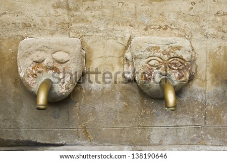 Human head fountain. Ancient stone fountain with two faces with metal pipe in the mouth, detail