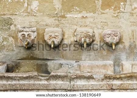 Human head fountain. Ancient stone fountain with four faces with metal pipe in the mouth