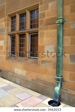 Victorian style limestone wall of the university with medieval style window and bronze rusty gutter