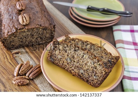 Slices of freshly baked banana nut bread with pecans sliced off a loaf of banana bread as it cools.