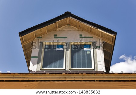A pair of windows have just been installed in a rooftop dormer window of a new building under construction. There is room for copy space in the sky.