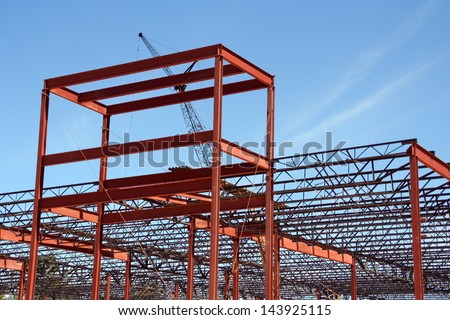 Ongoing framing and construction of a commercial shopping center. A crane can be seen in the background working to lift and maneuver large pieces of steel into place.
