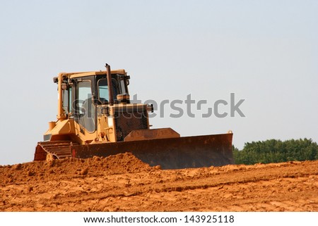 Dust rolls behind a bulldozer working to smooth out and level dirt on a commercial construction site.