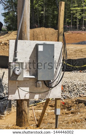 A telephone pole on a construction job site holds a temporary electrical panel and an electric meter for the work being done on the construction site.