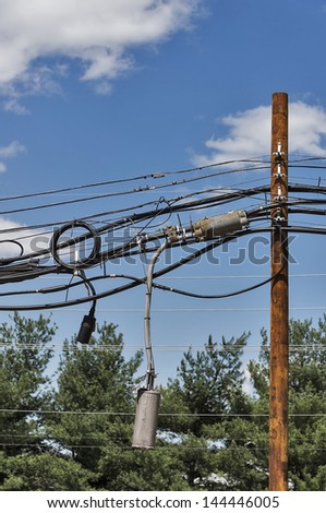 A wooden utility pole is burdened with an excessive amount of wires, cables and transformers. Copy space could be used in the sky.