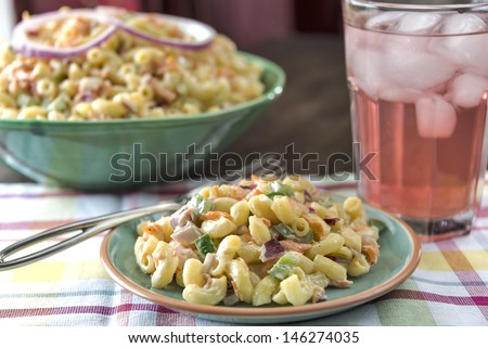 A plate full of traditional elbow macaroni salad is served with a refreshing glass of cold pink lemonade.