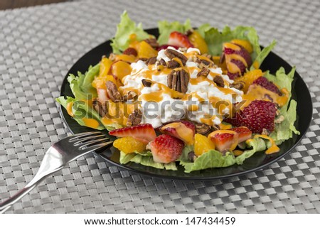 A colorful plate of refreshing fruit salad made with strawberries, mandarin oranges, cottage cheese, pecans and French dressing served over lettuce. One image in a series.