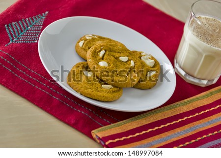 A plate full of soft, chewy pumpkin spice cookies served with a glass of traditional holiday egg nog on a Christmas themed place mat.