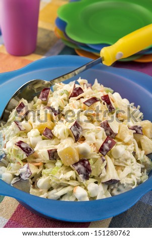 Ready for a summer picnic, a large bright bowl full of refreshing coleslaw is made with diced apples, marshmallows and pineapple chunks.