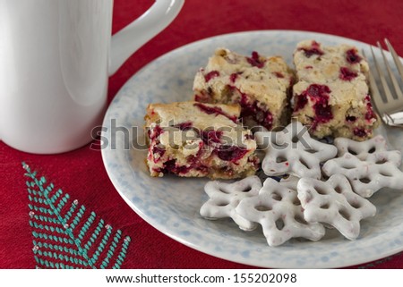 A large cup of coffee is served with a plate full of cranberry dessert cake and iced star shaped pretzels on a Christmas holiday placemat.