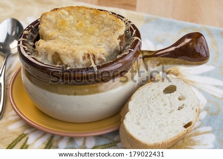 Traditional crock full of French onion soup topped with melted gruyere and served with French bread