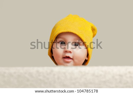 Cute Baby With A Beanie Hat Behind a Sofa