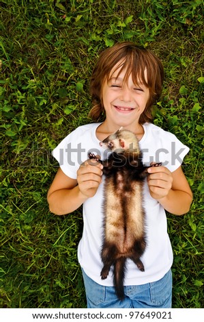 A lying on the grass smiling boy is hugging his pet