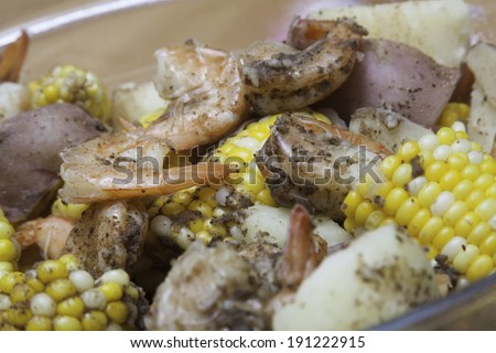 A glass bowl is filled with corn on the cob, red potatoes, and shrimp - a classic shrimp boil.  Everything is seasoned to perfection and steaming hot.  The photo has a shallow depth of field.