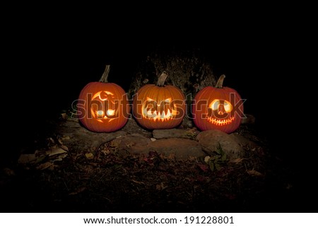 Three jack-o-lanterns sit on the ground outdoors, lighting the night. They are lit with candles and a light painting technique was used to provide additional light to the scene.