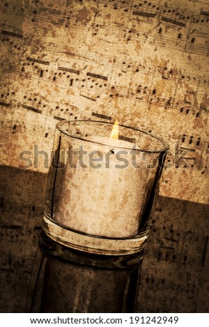 Old classical sheet music has a vintage tone and texture to it; vertical format; candle burning in foreground