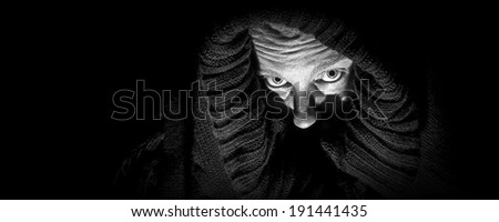 An ugly, scary looking woman in a black shroud; looks like she is  in despair; very shadowy harsh image; black and white panoramic format