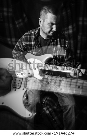 A man wearing a plaid flannel shirt plays an electric guitar; black and white photo; ghost image created using racking the lens technique