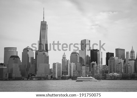 A black and white image of the Lower Manhattan Skyline with the World Trade Center Freedom Tower; the Spirit of New Jersey passes in the foreground on the Hudson River