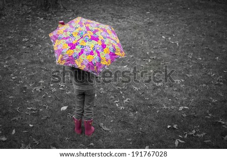 A little girl stands in the rain wearing bright pink rain boots and holding a bright flower umbrella.  Selective coloring