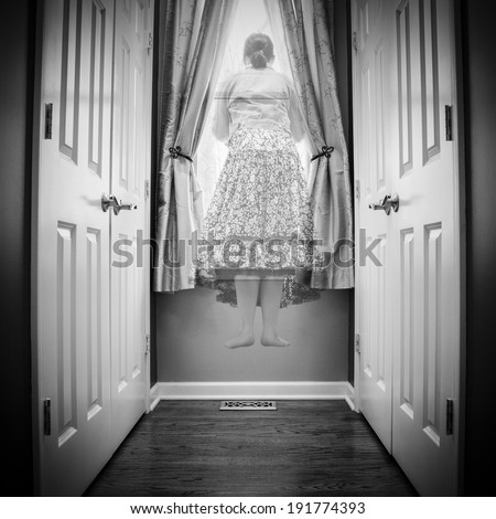 A see through figure of a female wearing a long flowing skirt, is seen floating above the floor and looking out of a window; between two sets of doors; monochrome image
