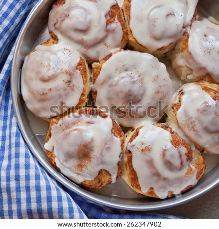 Cinnamon buns sit on a blue and white checked towel, straight from the oven. An icing glaze tops them.